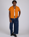 Isaac is wearing Pantry Button-Up in Creamsicle Orange and dark wash Denim Drop Pocket Pants