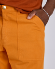 Close up of Isaac's hand in the front pocket of Work Pants in Creamsicle Orange