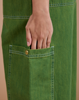 Anjaline has her hand on the side pant pocket of Denim Drop Pocket Pants in Green Overdye