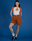 Alex is wearing Produce Raglan Tee in Habanero tucked into shorts
