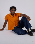 Isaac is wearing Pantry Button-Up in Creamsicle Orange and dark wash Denim Drop Pocket Pants