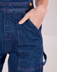Close up of Alex's hand in the front pocket of Carpenter Overalls in Dark Wash