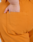 Close up of Juliet's hand in the back pocket of Work Pants in Creamsicle Orange