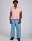 Isaac is wearing a buttoned up Pantry Button-Up in Baby Pink and light wash Denim Drop Pocket Pants