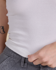 Alex is holding the hem of Racerback Tank in Vintage Tee White