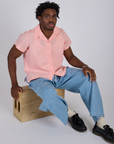Isaac is wearing Pantry Button-Up in Baby Pink and light wash Denim Drop Pocket Pants