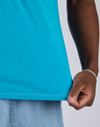 Close up of Isaac tugging the bottom hem of Jr. Varsity Tee in Hawaiian Blue