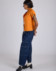 Side view of Pantry Button-Up in Creamsicle Orange and dark wash Denim Drop Pocket Pants on Kira