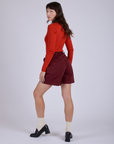 Angled back view of Pleated Trouser Shorts in Red Wineand mustang red Long Sleeve Gingham Baby Tee on Alex
