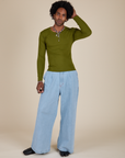 Jerrod is wearing Long Sleeve Baby Tee in Summer Olive and light wash Indigo Wide Leg Trousers