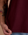 Burly Tee in Red Wine close up with Jesse holding the bottom hem