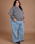 Angled front view of Burly Tee in Washed Grey and light wash Indigo Wide Leg Trousers on Sam