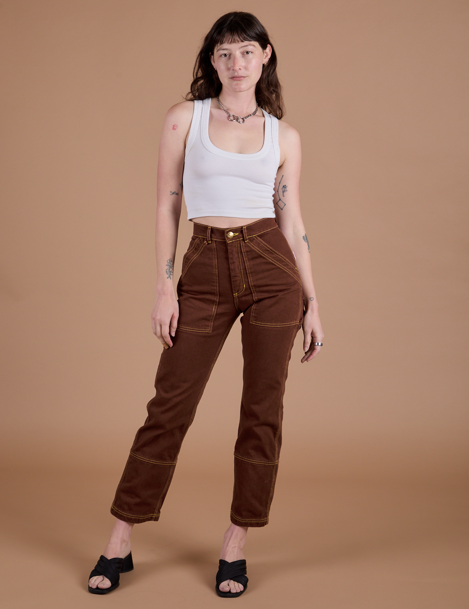 Alex is 5’8” and wearing XXS Carpenter Jeans in Fudgesicle Brown paired with a Cropped Tank in Vintage Tee White