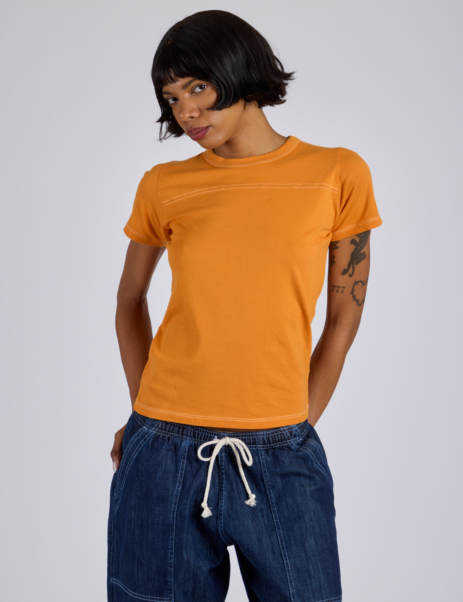 Kira is 5’10” and wearing P Jr. Varsity Tee in Creamsicle Orange