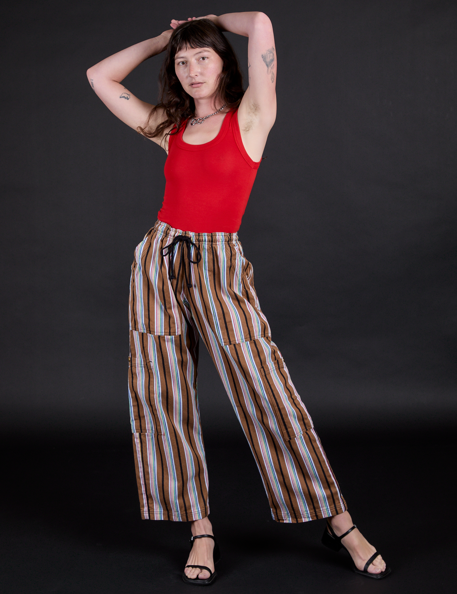 Alex is 5’8” and wearing XXS Striped Drop Pocket Pants in Retro Rainbow paired with mustang red Racerback Tank