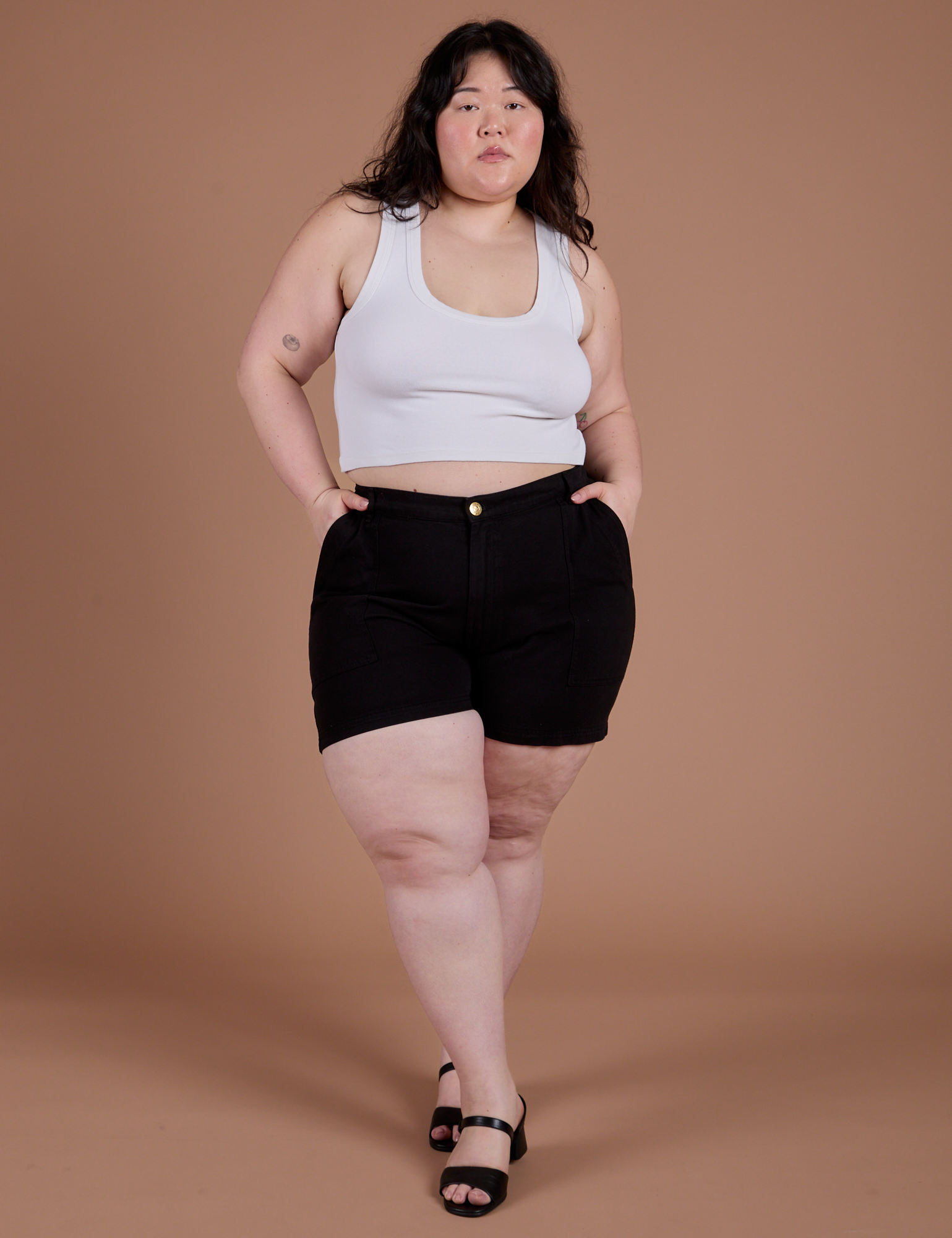 Ashley is 5’7” and wearing 1XL Classic Work Shorts in Basic Black paired with a Cropped Tank in Vintage Tee White