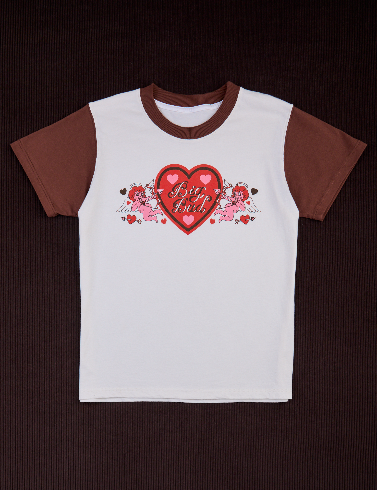White body with fudgesicle brown sleeves and neckline. Large red heart with black inner outline and pink hearts. Big Bud text in center of red heart. Two pink cupids with red hair are pointing arrows to the heart.