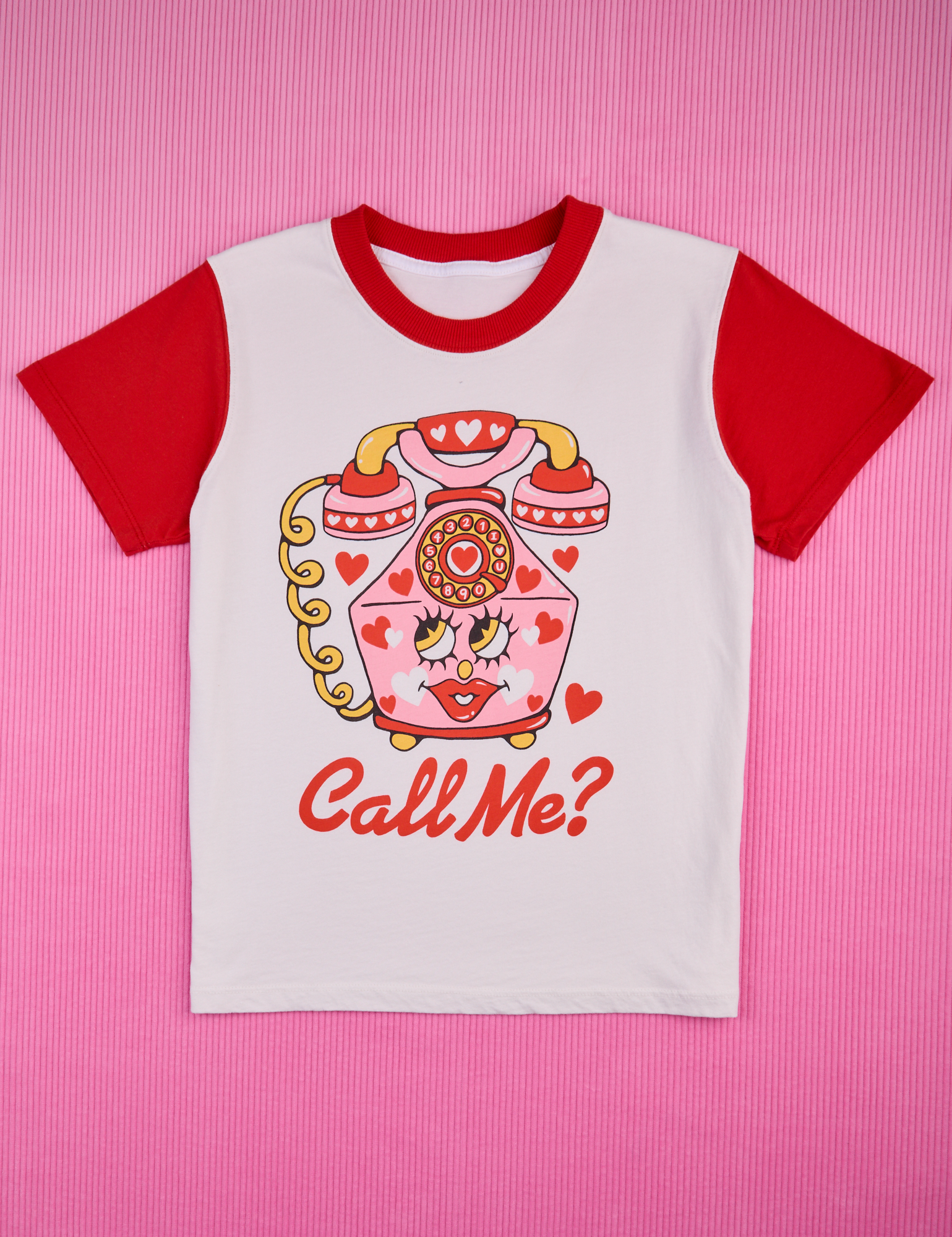 White body with mustang red sleeves and neckline. Illustration of a pink vintage phone with red hearts in the center. Phone has a face with red lips. Call Me? text below in red.