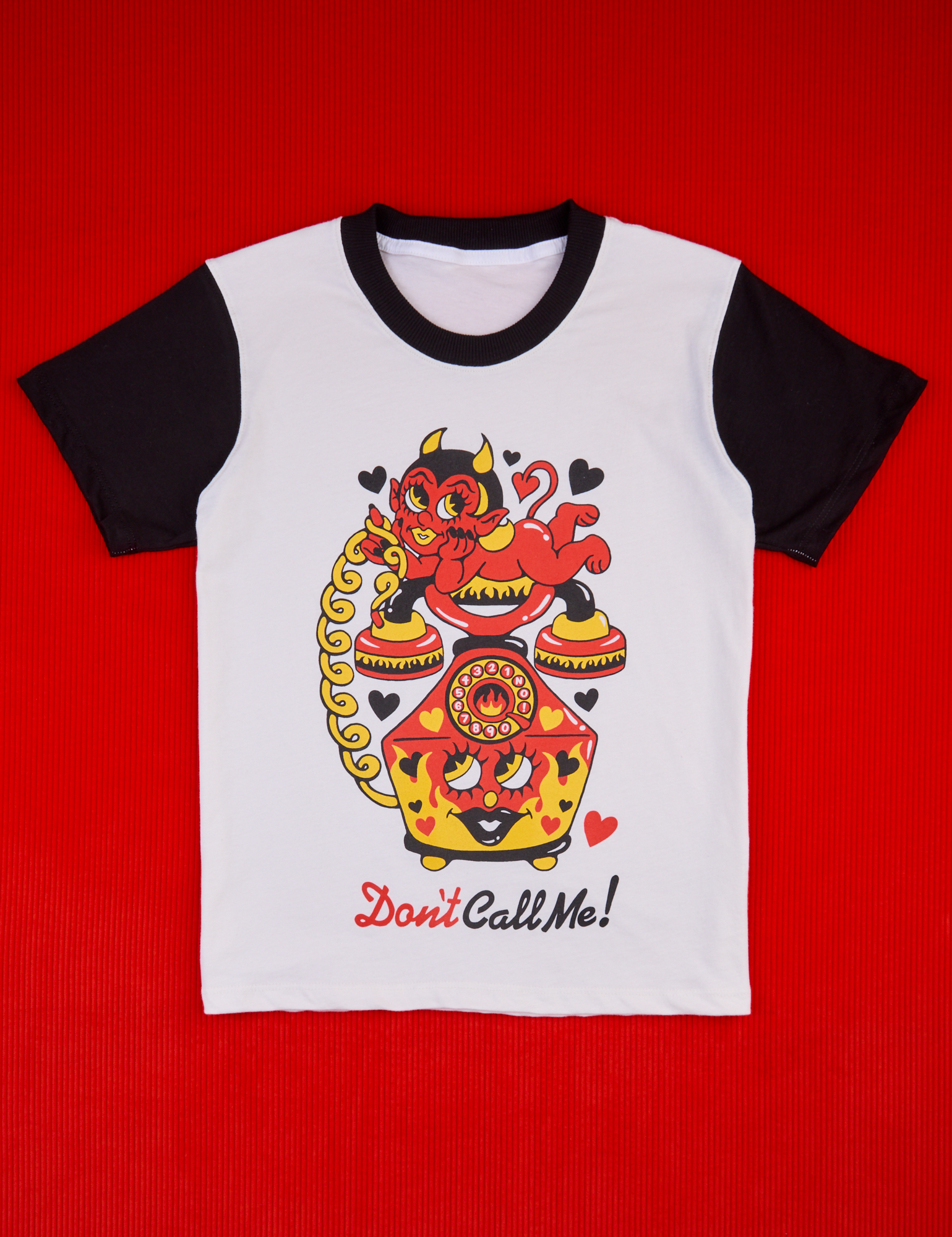 White body with black sleeves and neckline. Illustrated yellow, red and black vintage phone. Red devil lays on the receiver. Don't Call Me text in red and black below. 