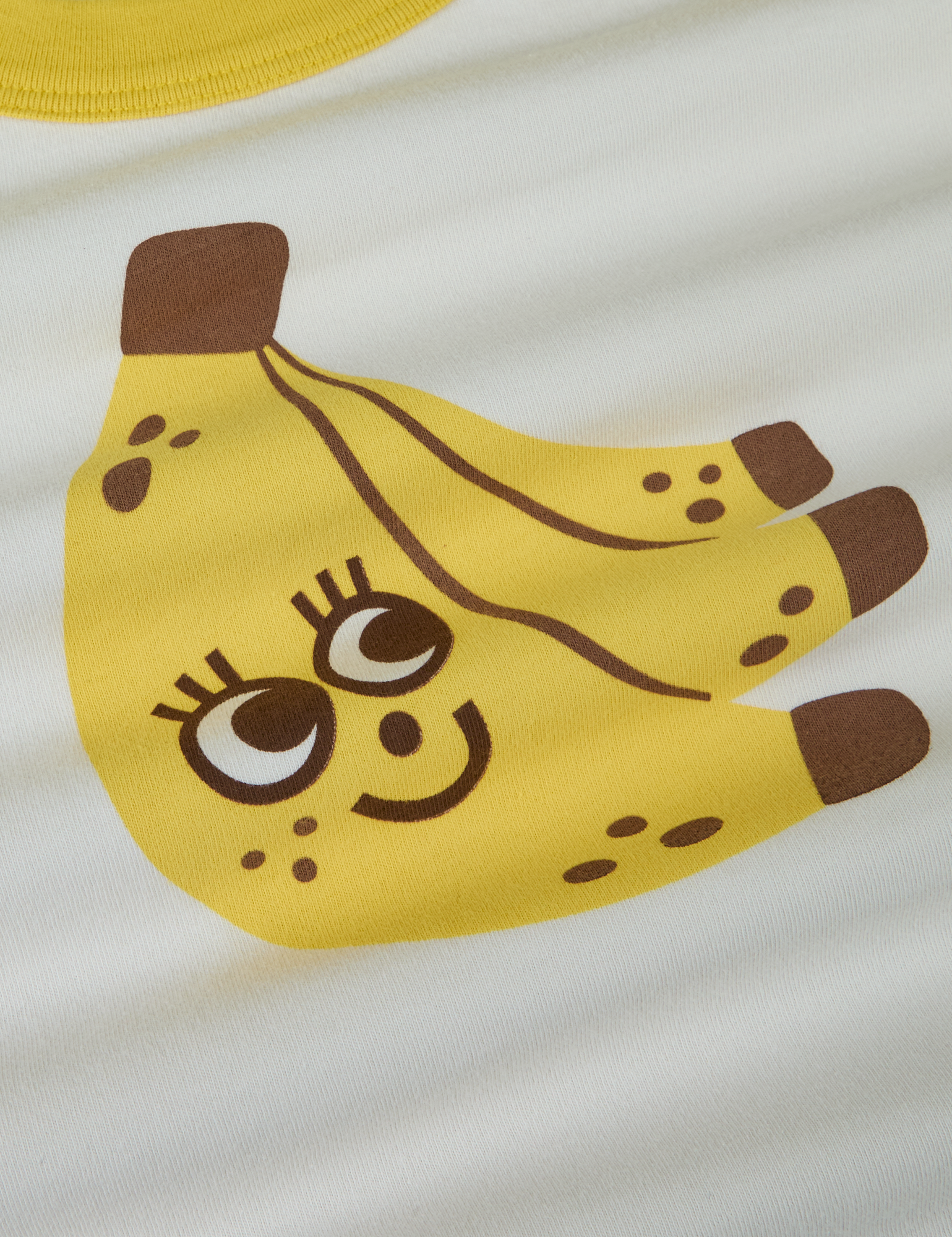 Produce Raglan Tee in Banana close up. Illustrated banana character in yellow and brown