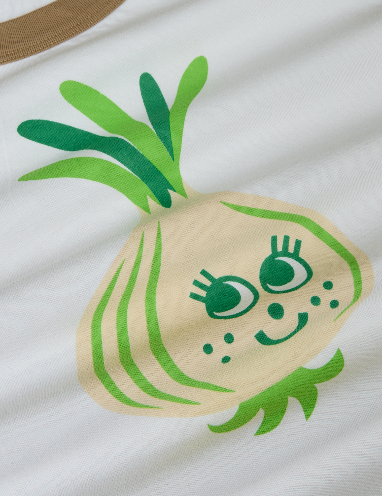 Produce Raglan Tee in Onion close up. Illustrated onion character in off-white and green