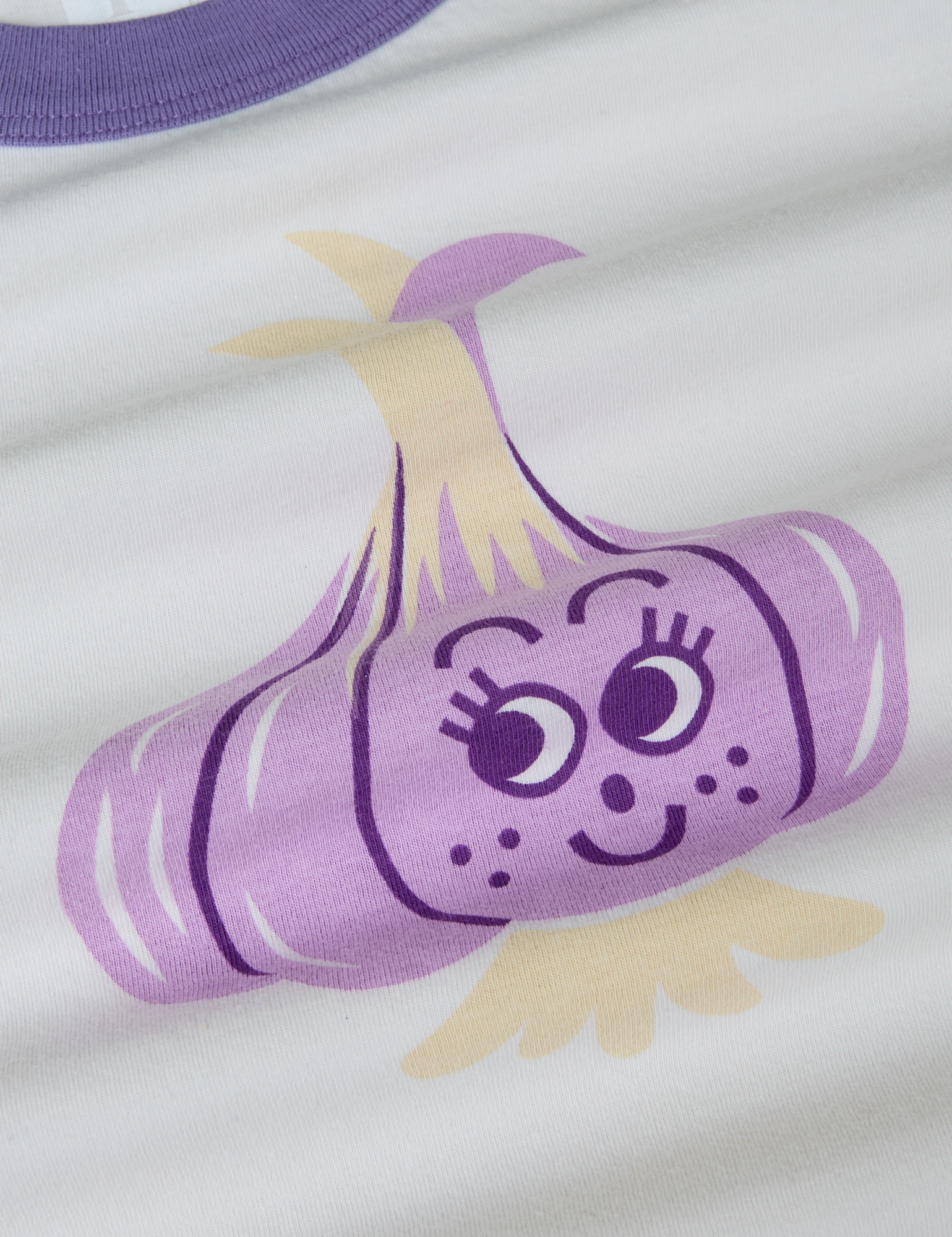 Produce Raglan Tee in Garlic close up. Illustrated garlic character in purple and off-white