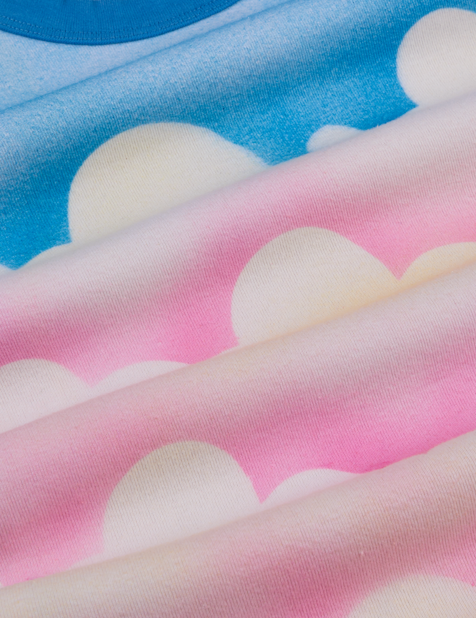 Airbrush Cloud Baby Tee fabric detail close up. Pink and blue background with white clouds