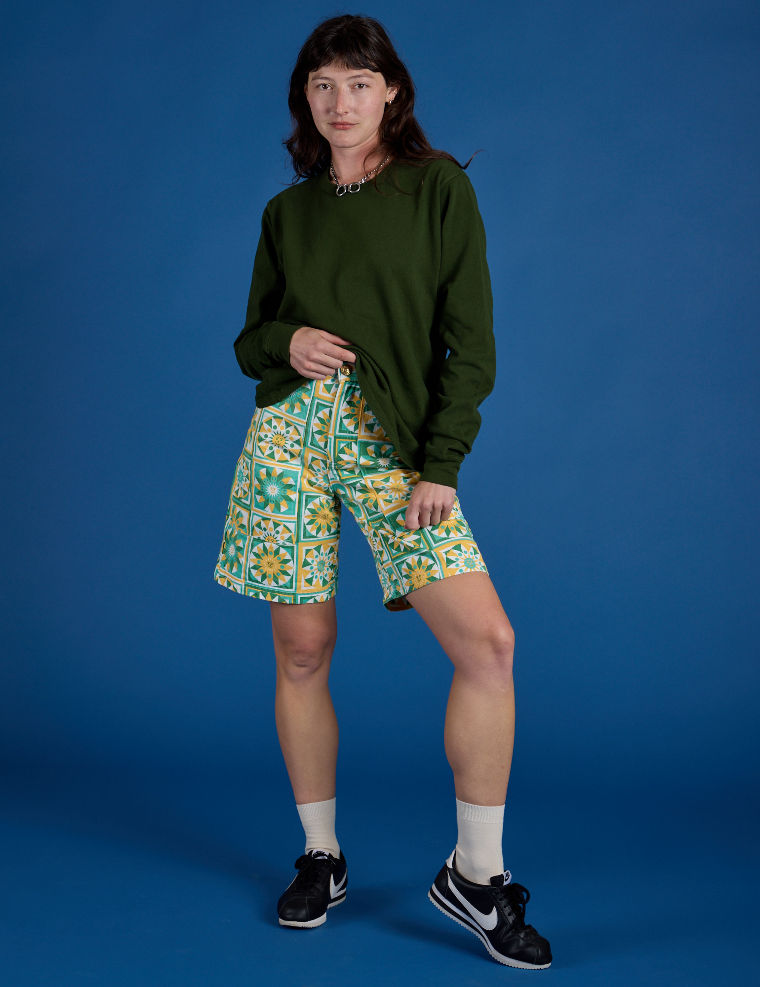 Alex is wearing Longline Work Shorts in Spring Quilt Print and evergreen Long Sleeve Burly Tee