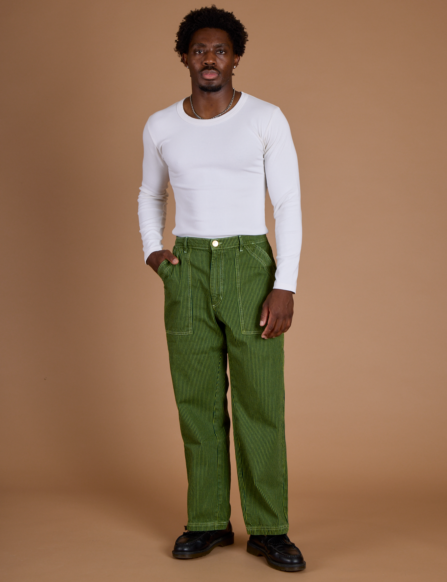 Isaac is wearing Railroad Denim Work Pants in Gross Green Overdye and vintage tee white Long Sleeve Baby Tee