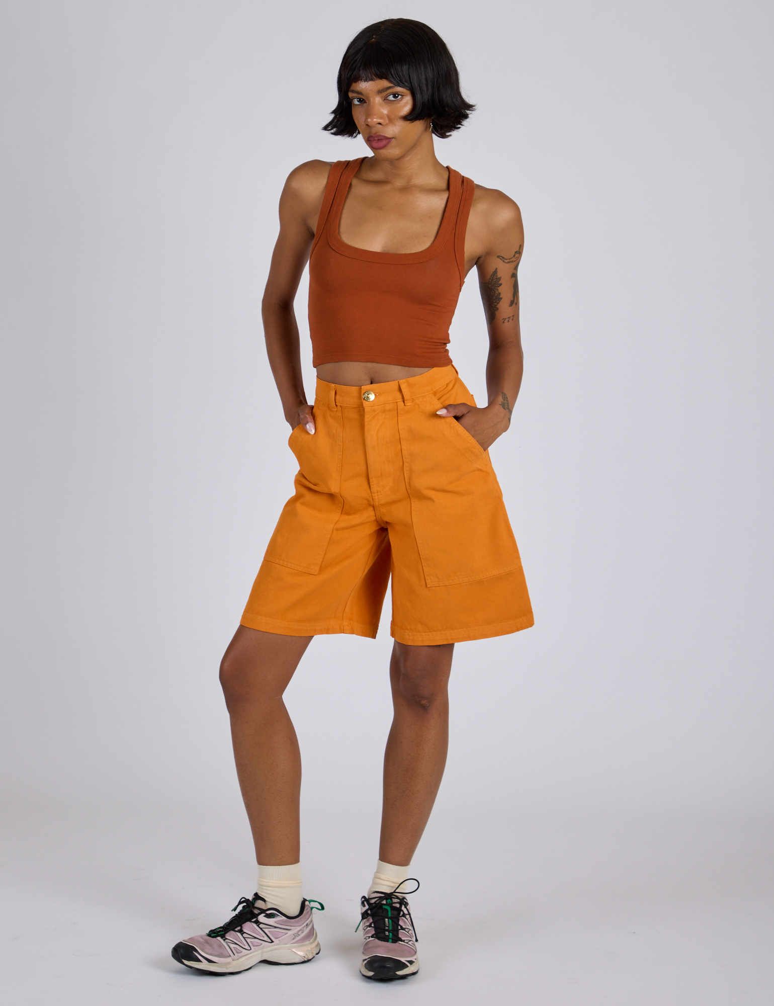 Kira is wearing Longline Work Shorts in Creamsicle Orange and burnt terracotta Cropped Tank