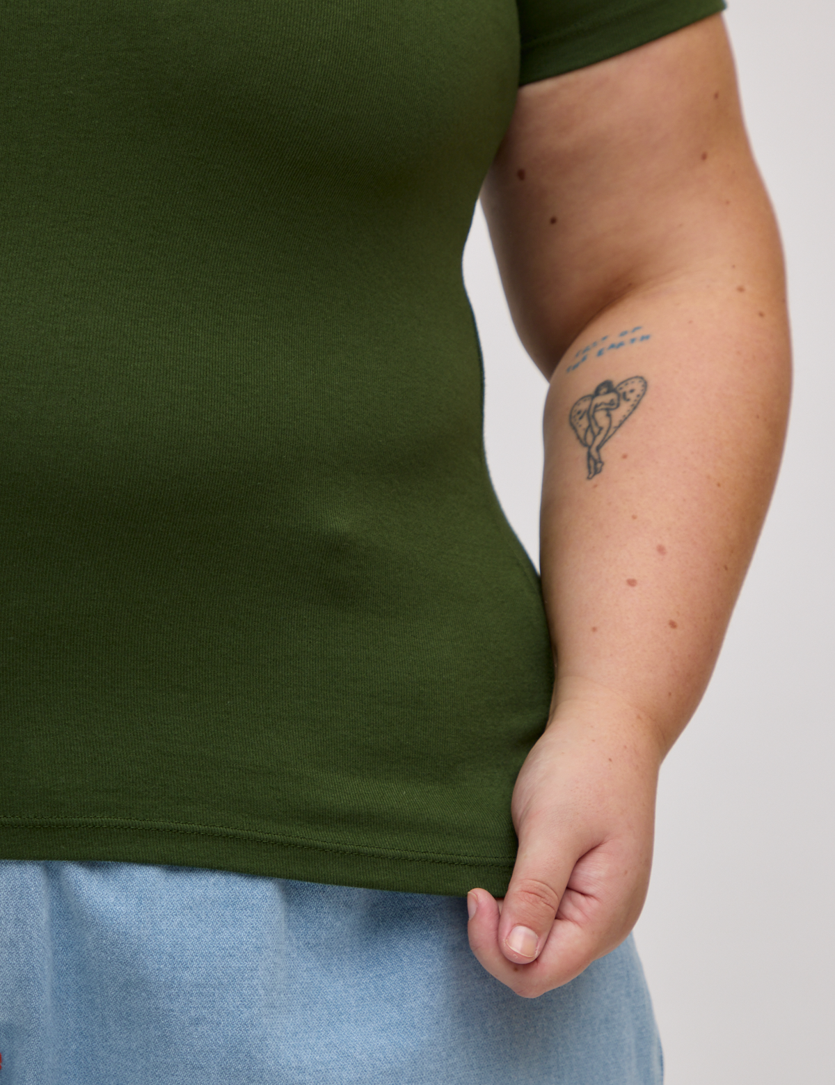 Close up of Juliet holding the Baby Tee in Evergreen bottom hem