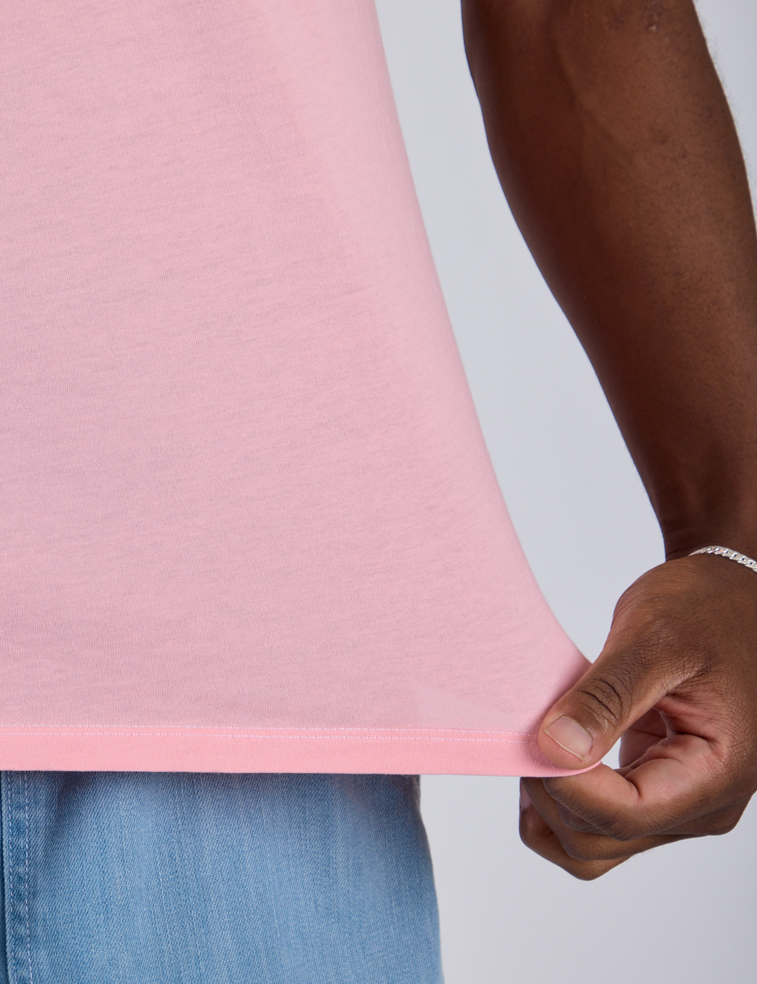 Close up of Isaac pulling on the bottom hem of Jr. Varsity Tee in Baby Pink