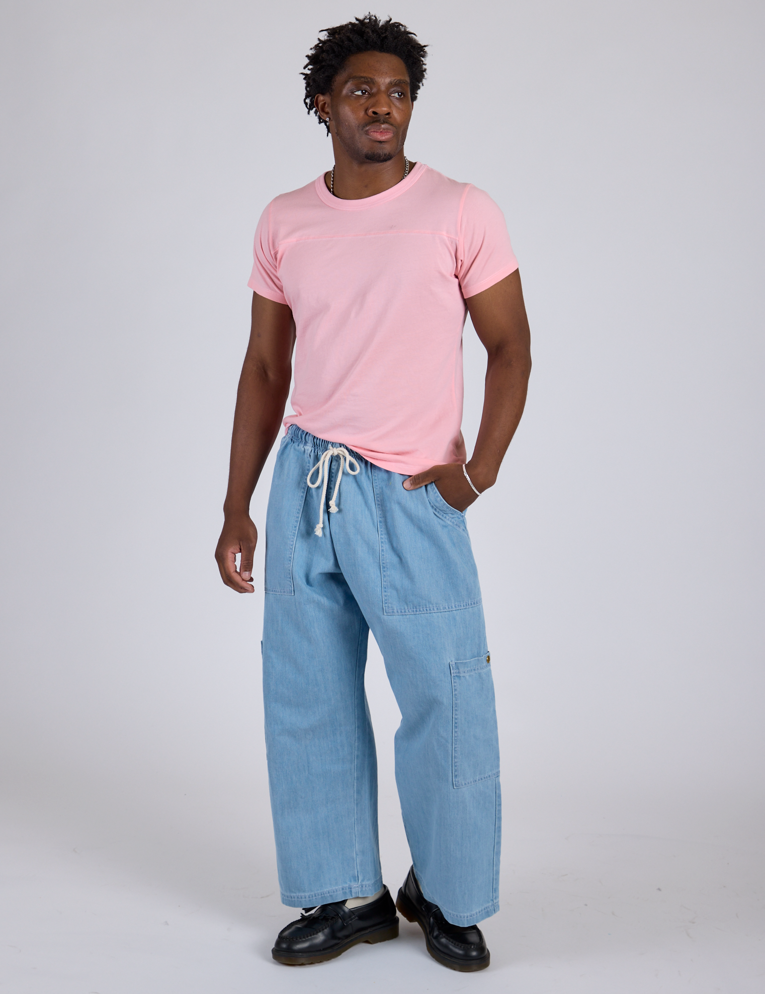 Isaac is wearing Jr. Varsity Tee in Baby Pink paired with light wash Denim Drop Pocket Pants