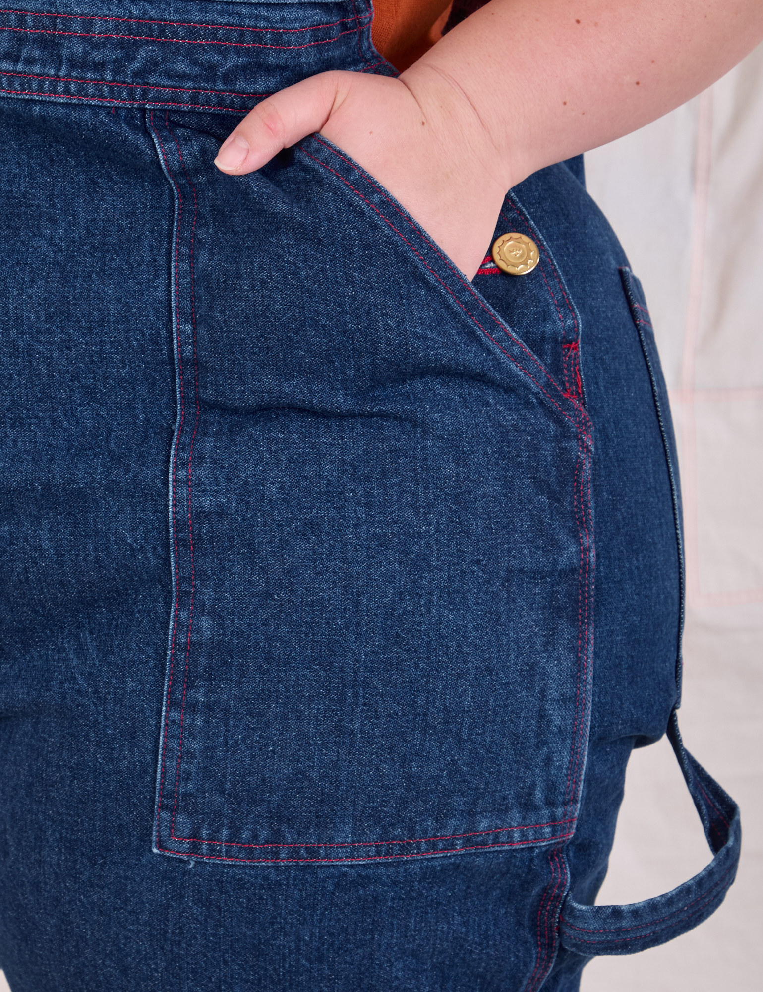 Close up of Ashley's hand in the front pocket of Carpenter Overalls in Dark Wash