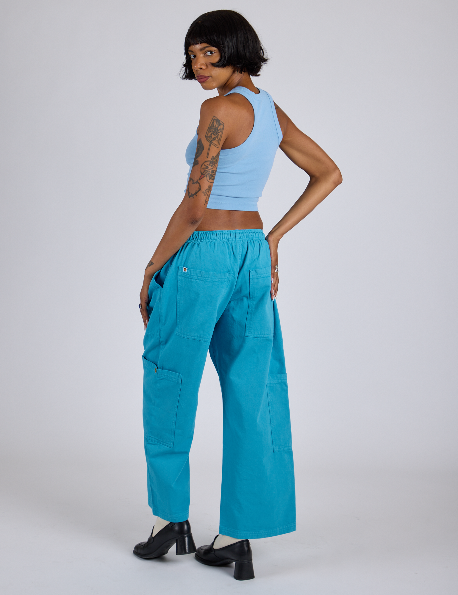 Angled back view of Drop Pocket Cargo Pants in Hawaiian Blue and baby blue Racerback Tank on Kira