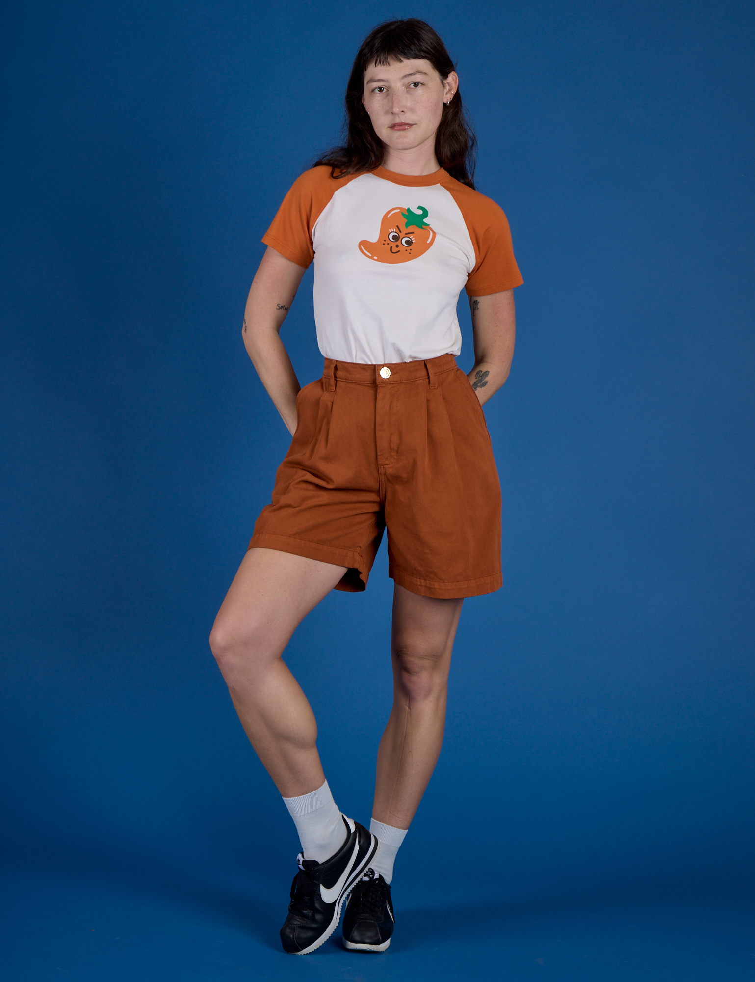 Alex is wearing Produce Raglan Tee in Habanero tucked into shorts