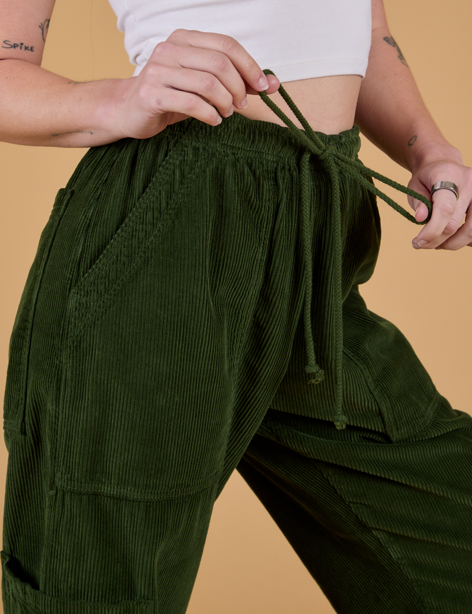 Close up of Corduroy Drop Pocket Cargo Pants in Evergreen with Alex tugging on the drawstring