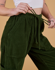 Close up of Corduroy Drop Pocket Cargo Pants in Evergreen with Alex tugging on the drawstring