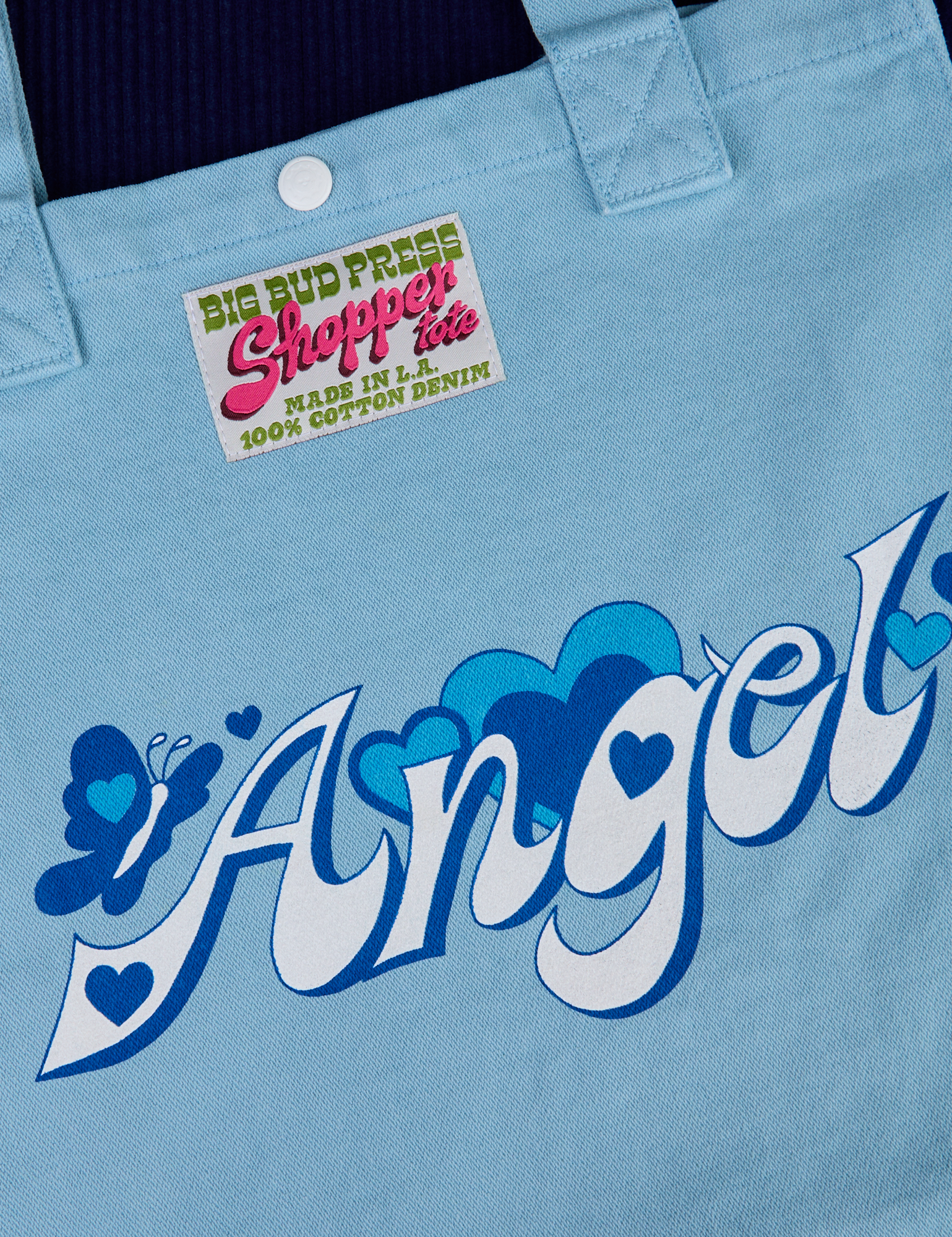 Shopper Tote close up with Angel text in white and blue shadows. A butterfly next to it and hearts surrounding text. 