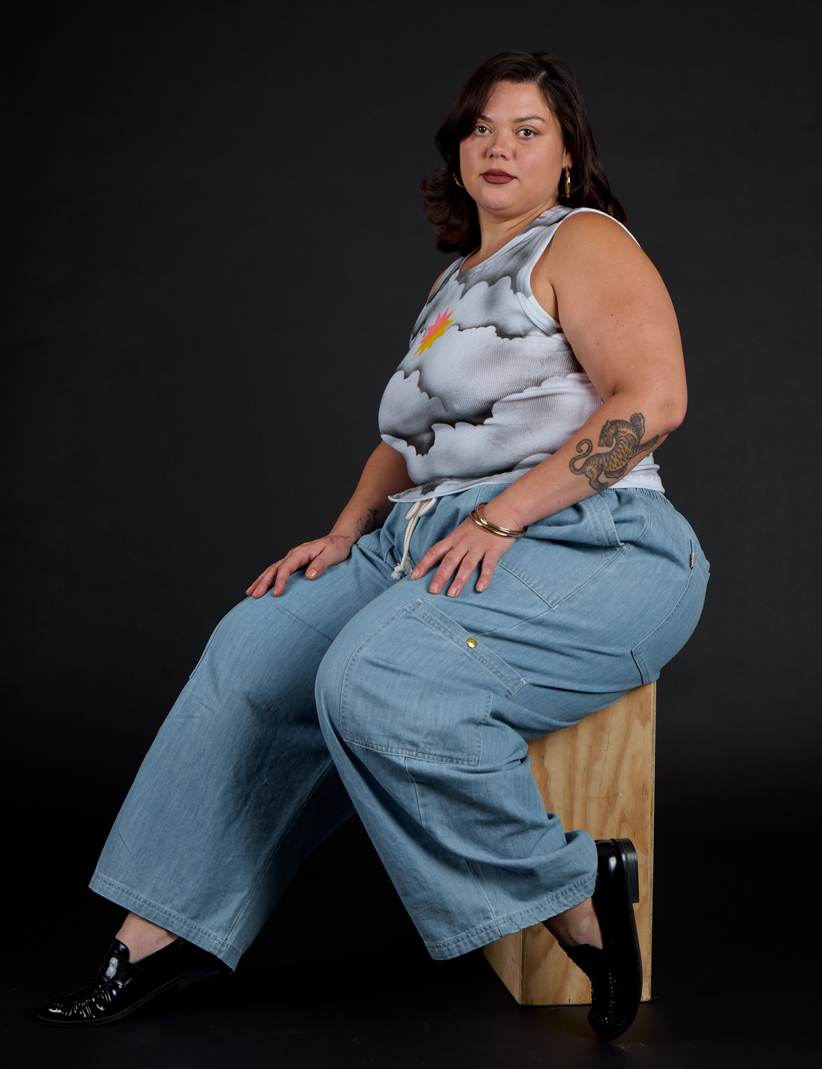 Side view of the Dark Cloud Airbrush Muscle Tee and Light Wash Denim Drop Pocket Cargo Pants worn by Kristen