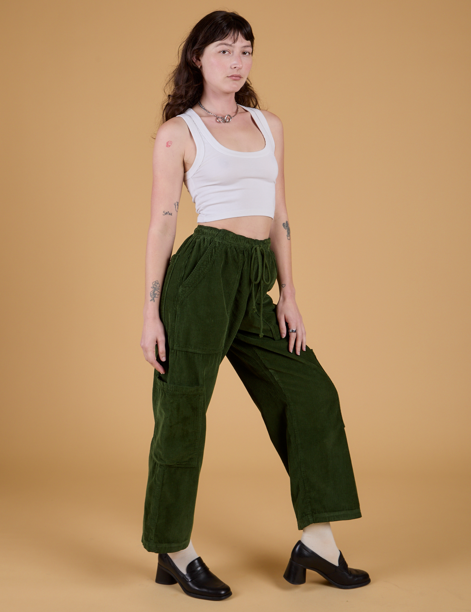Angled front view of Corduroy Drop Pocket Cargo Pants in Evergreen and Cropped Tank in Vintage Tee White on Alex