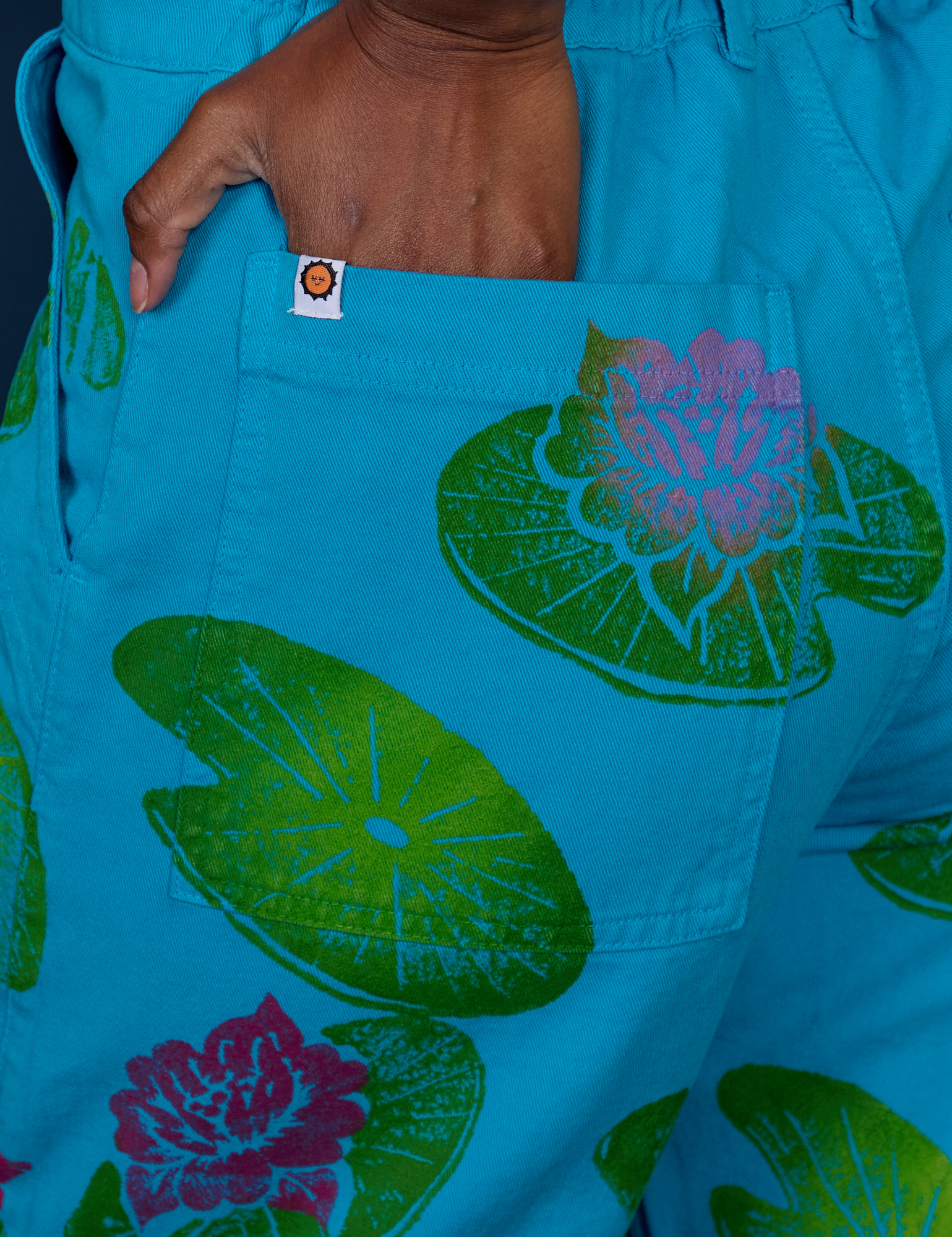 Close up of Kandia's hand in the back pocket of Paintstamped Work Pants in Lilypad