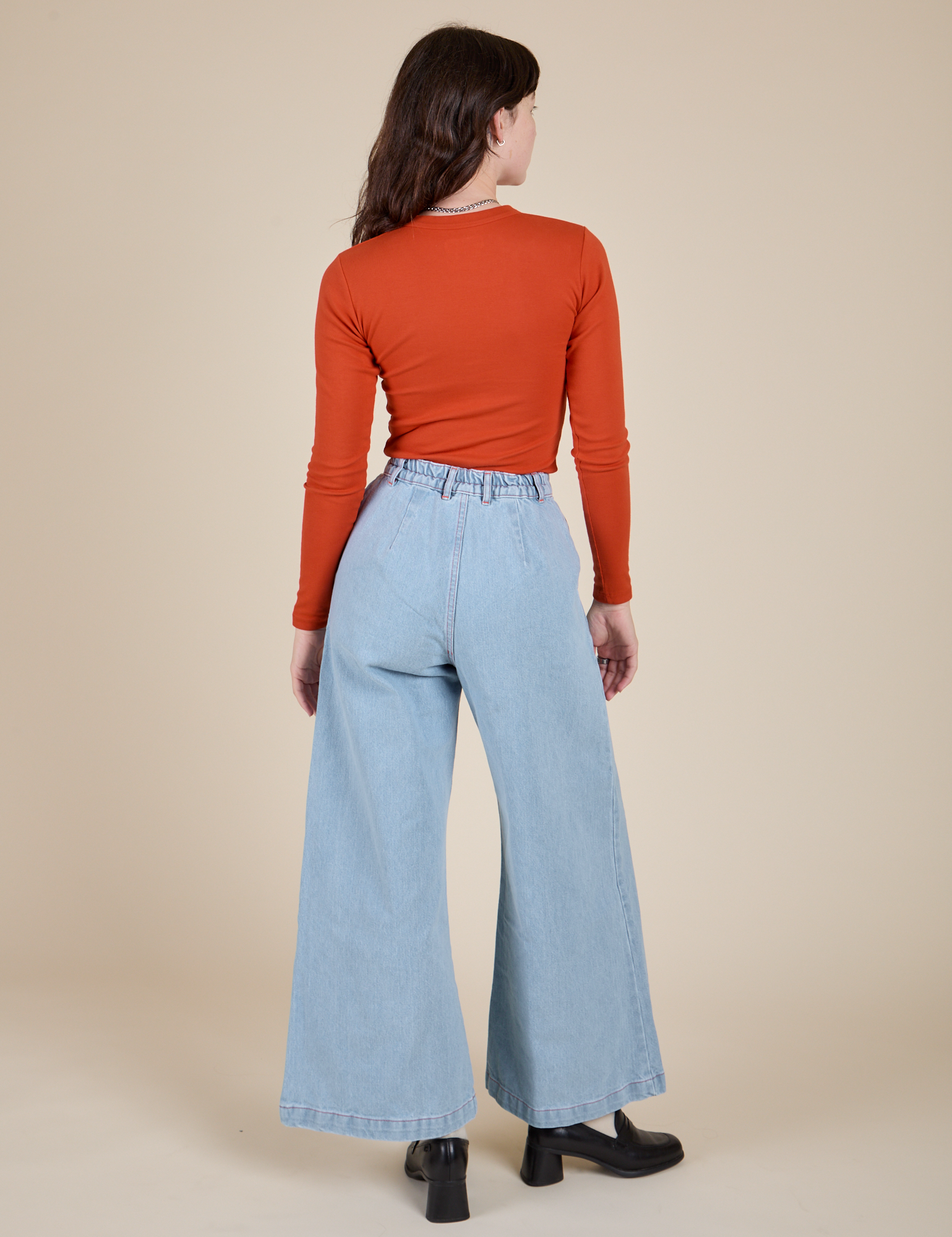 Back view of Long Sleeve Baby Tee in Chili Red and light wash Indigo Wide Leg Trousers on Alex