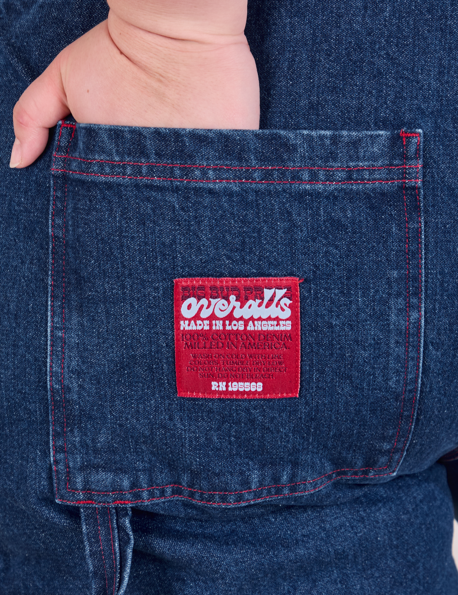 Close up of Ashley's hand in the back pocket of Carpenter Overalls in Dark Wash