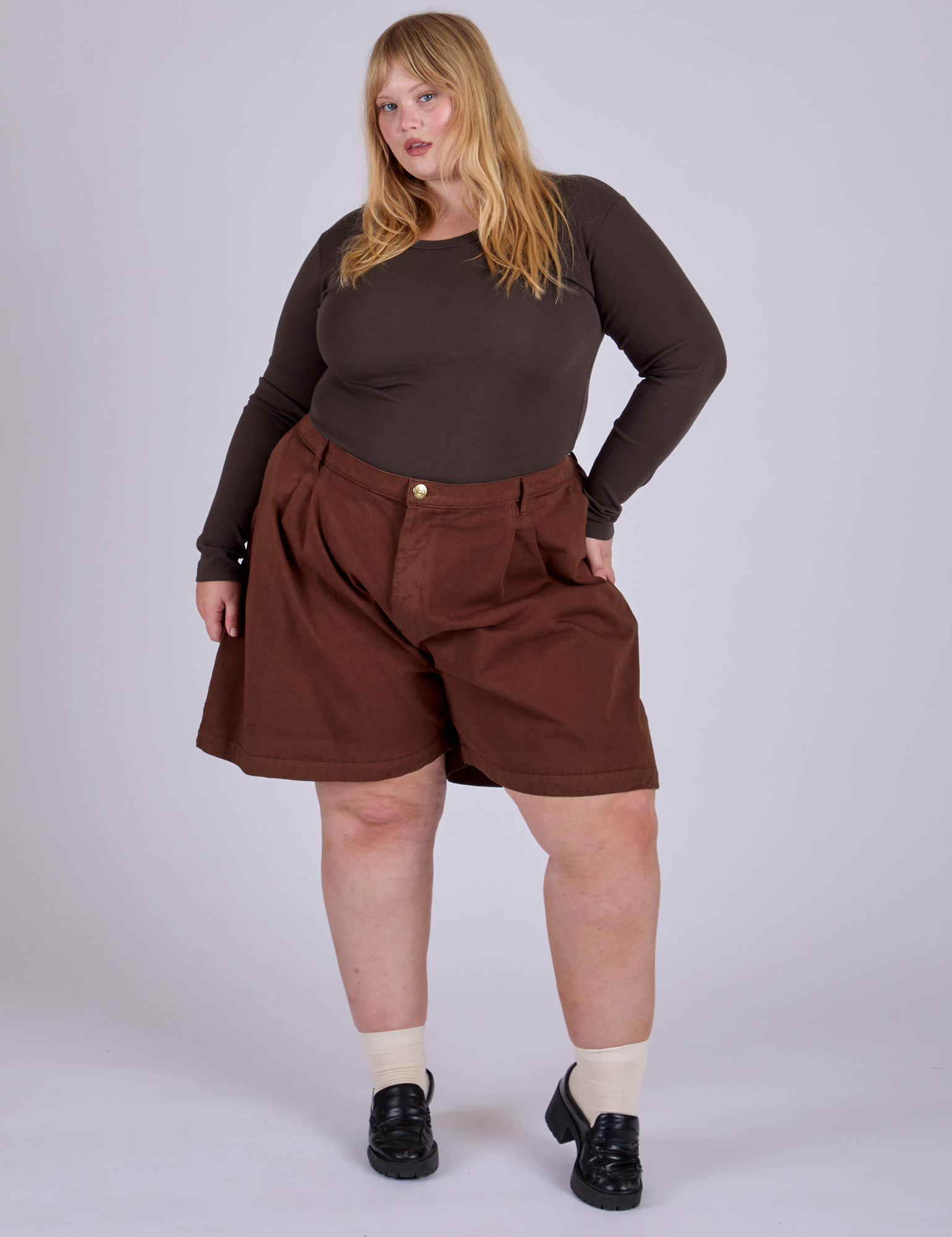 Juliet is 5’7” and wearing 2XL Pleated Trouser Shorts in Fudgesicle Brown paired with espresso brown Long Sleeve Baby Tee