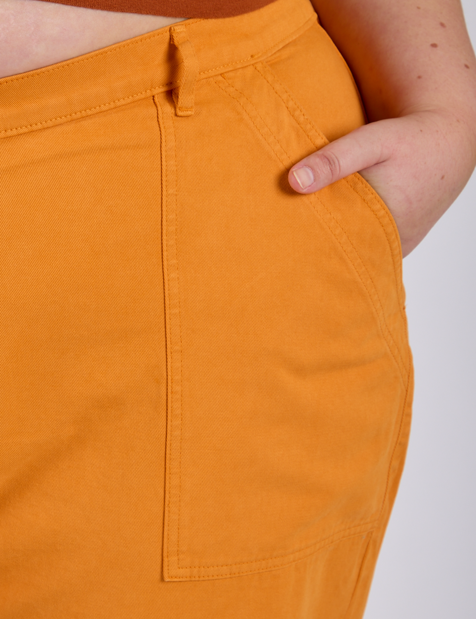 Close up of Juliet's hand in the front pocket of  Work Pants in Creamsicle Orange