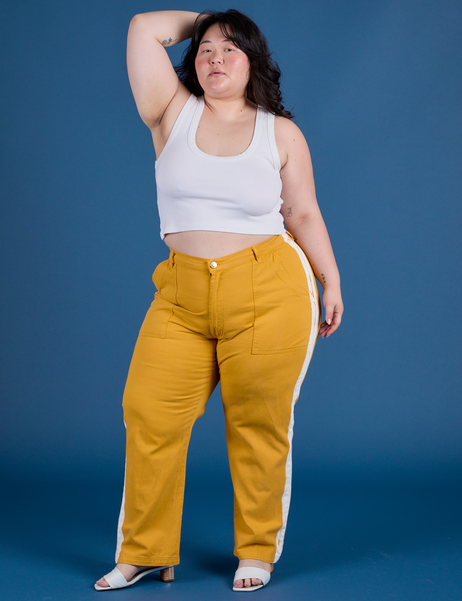 Ashley is 5’7” and wearing 1XL Painted Work Pants in Mustard Yellow paired with vintage tee white Cropped Tank
