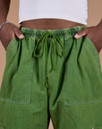 Isaac has both hands in the front pockets of Denim Drop Pocket Pants in Green Overdye