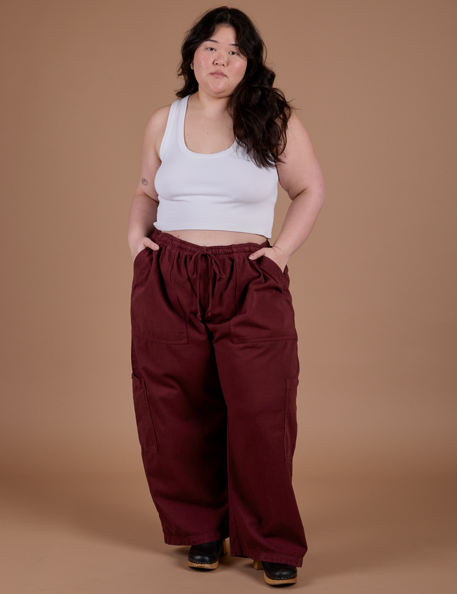 Ashley is 5'7" and wearing 1XL Drop Pocket Cargo Pants in Red Wine paired with vintage tee white Cropped Tank