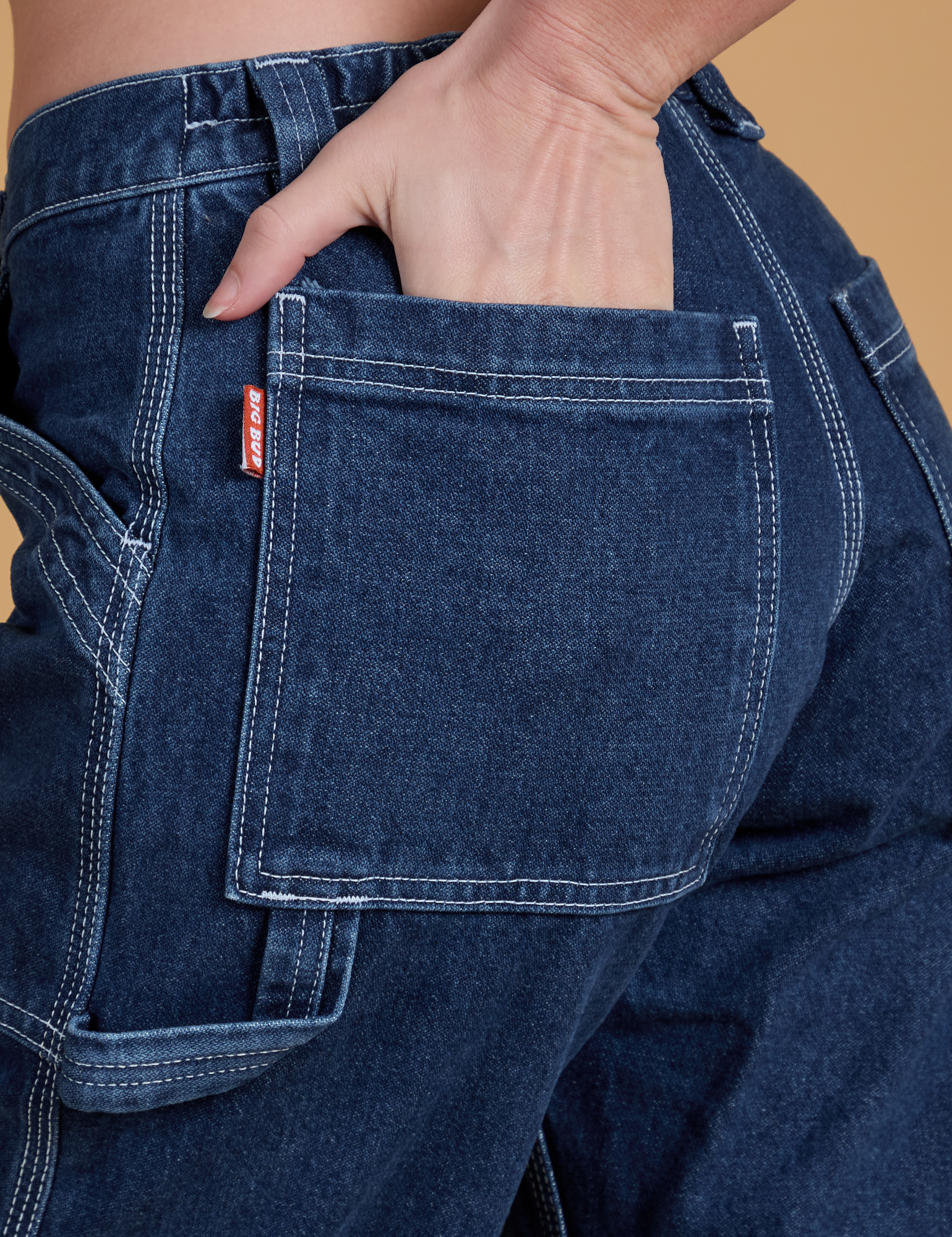 Close up of Alex's hand in the back pocket of Mid-Rise Carpenter Jeans in Dark Wash